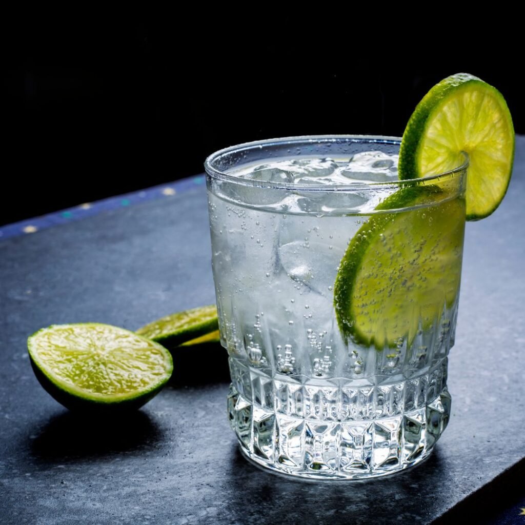 A clear glass of water with fresh lime slices resting on the side, reflecting light in a bright setting.
